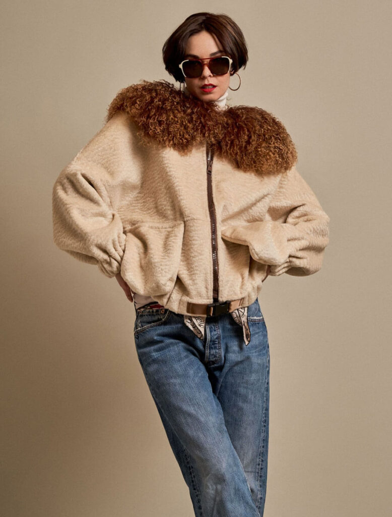 Mujer posando con chaqueta beige de astracán y gafas de sol, en look casual.