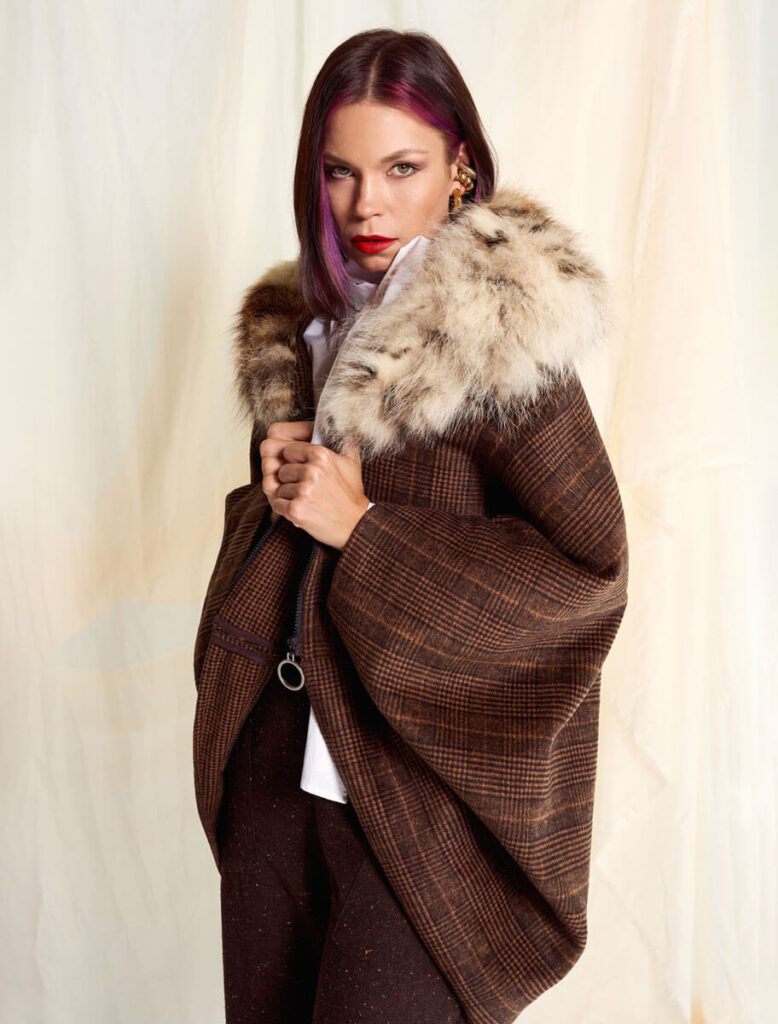 Modelo luciendo la Capa Mimosa Cuadro Marrón con cuello de zorro natural, vista frontal con actitud elegante.